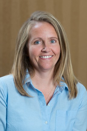 A photograph of a smiling woman wearing a blue shirt.