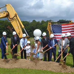 Men, women, and children wearing construction hats using shovels to break ground