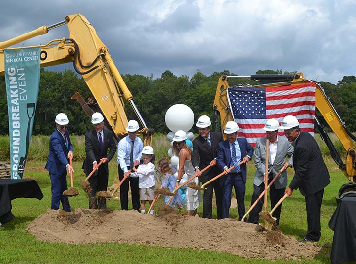 Men, women, and children wearing construction hats using shovels to break ground