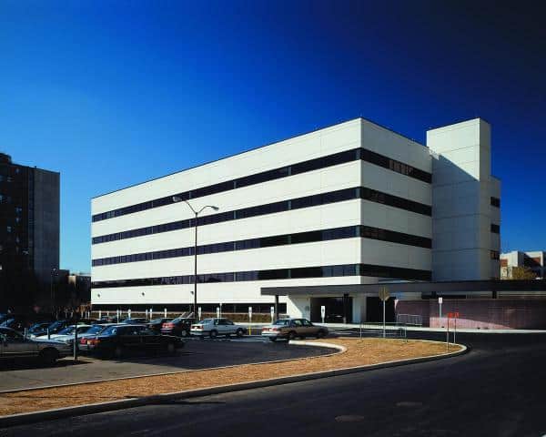 Exterior building of the University of Medicine and Dentistry in New Jersey next to a parking lot full of cars and a light post.