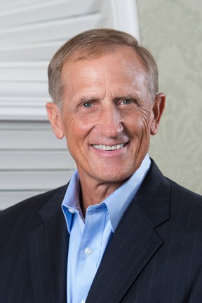A close photo of a man smiling, wearing a suit.