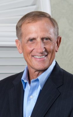 A close photo of a man smiling, wearing a suit.