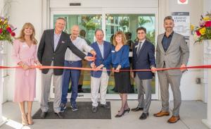 A group of people holding on to a red ribbon and cutting it with red scissors.